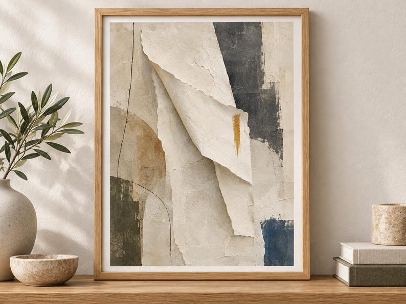 May include: A framed abstract wall art print featuring layered paper-like textures in shades of beige, cream, and charcoal gray. The composition includes a central folded element, a thin black line, and a small vertical gold brushstroke accent.