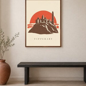 May include: A framed wall art print featuring a stylized illustration of the Rock of Cashel in Tipperary. The design shows a dark brown silhouette of the stone ruins against a large, solid orange sun on a cream background with the text TIPPERARY.
