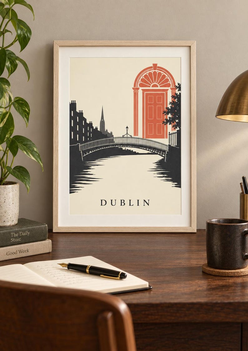 K&ouml;nnte beinhalten: Ein gerahmter Kunstdruck mit einer stilisierten Illustration von Dublin, Irland. Die Grafik zeigt eine dunkelgraue Bogenbr&uuml;cke &uuml;ber einem Fluss, eine Stadtsilhouette und eine markante korallenfarbene georgianische T&uuml;r. Das Wort DUBLIN steht unten.