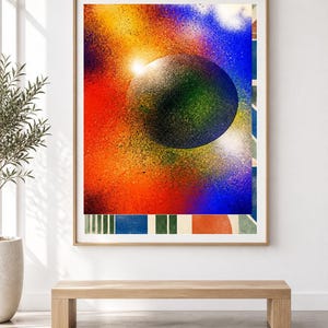 Op de afbeelding: Een ingelijste rechthoekige wandkunstprint met een grote, donkere, getextureerde bol gecentreerd tegen een levendige, met spuitverf bewerkte achtergrond van rood, oranje, geel en blauw. De onderrand toont een reeks verticale strepen en geometrische vormen.