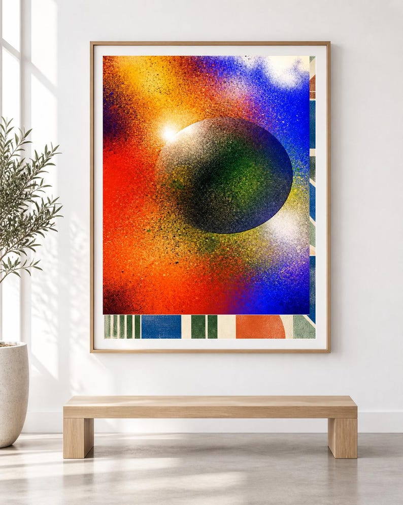 Op de afbeelding: Een ingelijste rechthoekige wandkunstprint met een grote, donkere, getextureerde bol gecentreerd tegen een levendige, met spuitverf bewerkte achtergrond van rood, oranje, geel en blauw. De onderrand toont een reeks verticale strepen en geometrische vormen.