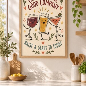 May include: A framed wall art print featuring a cartoon illustration of a wine glass, a beer glass, and a martini glass with faces. The text reads "GOOD DRINKS, GOOD COMPANY" and "RAISE A GLASS TO TODAY" in a cream-colored background with decorative leaves.