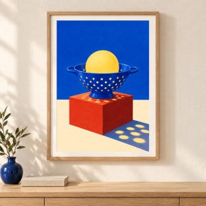 Puede incluir: Una l&aacute;mina art&iacute;stica enmarcada que muestra un colador azul vibrante sobre un cubo rojo s&oacute;lido. Dentro del colador hay una esfera amarilla grande y lisa. La composici&oacute;n se sit&uacute;a sobre un fondo azul intenso con un primer plano de color crema.