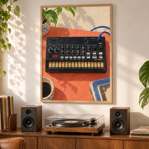 Puede incluir: Una impresi&oacute;n de arte mural enmarcada que representa una caja de ritmos anal&oacute;gica Korg Volca Beats negra sobre una superficie naranja vibrante, con una pantalla digital que muestra 120, perillas de control, teclado t&aacute;ctil y un cable azul.