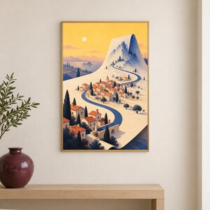 May include: A framed vertical wall art print depicting a Mediterranean-style village with terracotta-roofed buildings nestled at the base of a large, snow-capped mountain peak under a warm yellow sky with a winding blue road leading upward.