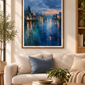 May include: A framed wall art print featuring an impressionistic cityscape at twilight. The painting displays a dark blue sky and water, with warm orange and yellow lights reflecting from the buildings onto the surface of the water below.