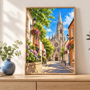 Pu&ograve; includere: Una stampa artistica incorniciata che raffigura una soleggiata strada europea con un'alta chiesa in pietra dotata di guglia e rosone, fiancheggiata da edifici in mattoni, cesti di fiori appesi e vivaci cespugli di ortensie blu, rosa e viola.