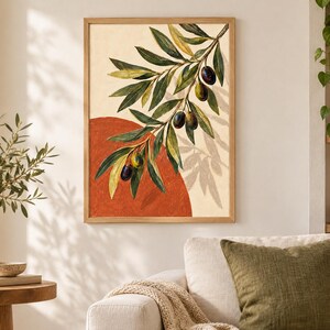 May include: A framed wall art print featuring a painted olive branch with green leaves and dark olives against a cream background. A large, solid terracotta-colored circle is positioned behind the branch, creating a layered, graphic composition.