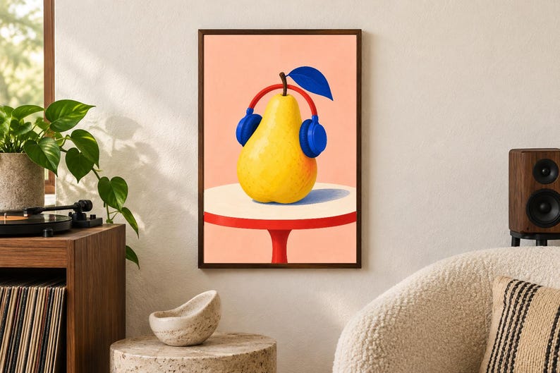 May include: A framed wall art print featuring a bright yellow pear wearing large blue headphones. The pear sits on a round white tabletop with a red base, set against a solid light peach background. A single dark blue leaf extends from the top.
