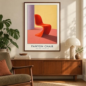 May include: A framed wall art print featuring a vibrant orange S-shaped chair set against a yellow wall and a pink floor, with a purple column on the left. The text PANTON CHAIR and Verner Panton is printed in black at the bottom of the poster.