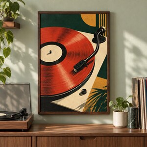 May include: A framed wall art print featuring a stylized illustration of a red vinyl record on a turntable. The composition includes geometric shapes in dark green, cream, and yellow, with a black tonearm resting on the record surface.