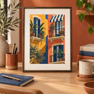 May include: A framed art print featuring a vibrant illustration of Mediterranean-style building facades with yellow and orange walls, blue shutters, wrought iron balconies, potted plants, and a striped awning, presented in a dark metallic frame.