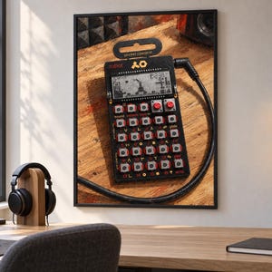 May include: A black Teenage Engineering PO-28 Robot pocket operator synthesiser featuring a monochrome LCD screen, a grid of silver buttons with red accents, and a black audio cable plugged into the top right corner of the device.