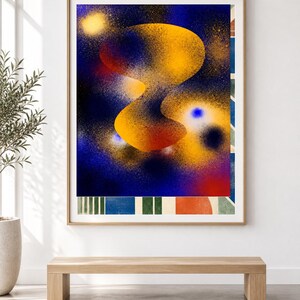 May include: A framed rectangular wall art print featuring a central abstract yellow and orange organic shape against a deep blue spray-painted background. The bottom section displays a series of vertical stripes in green, blue, and orange tones.