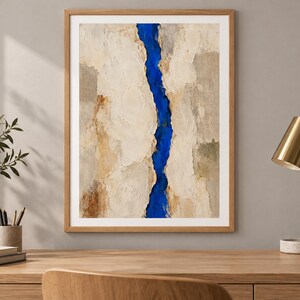 May include: A framed rectangular wall art piece featuring a vertical, jagged, deep blue central fissure that divides textured, layered panels of beige, cream, and light brown tones, encased in a simple, light-colored wooden frame.