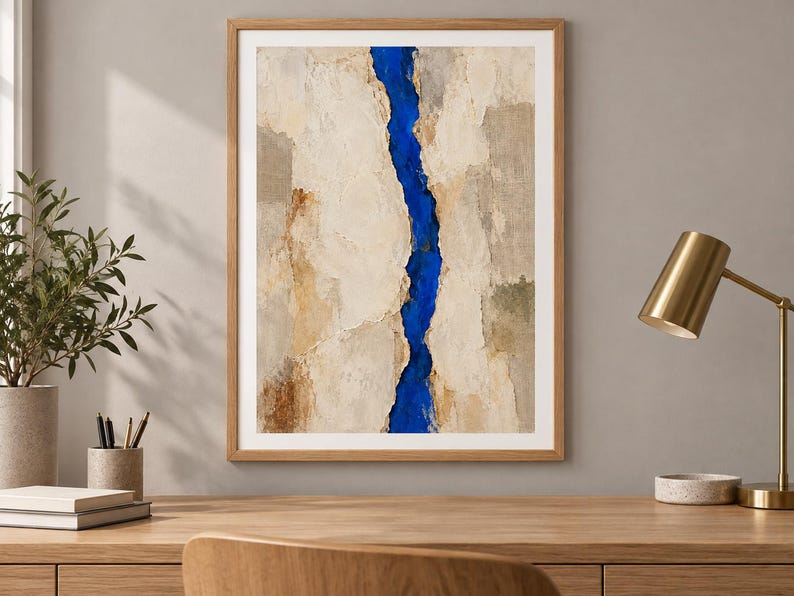 May include: A framed rectangular wall art piece featuring a vertical, jagged, deep blue central fissure that divides textured, layered panels of beige, cream, and light brown tones, encased in a simple, light-colored wooden frame.