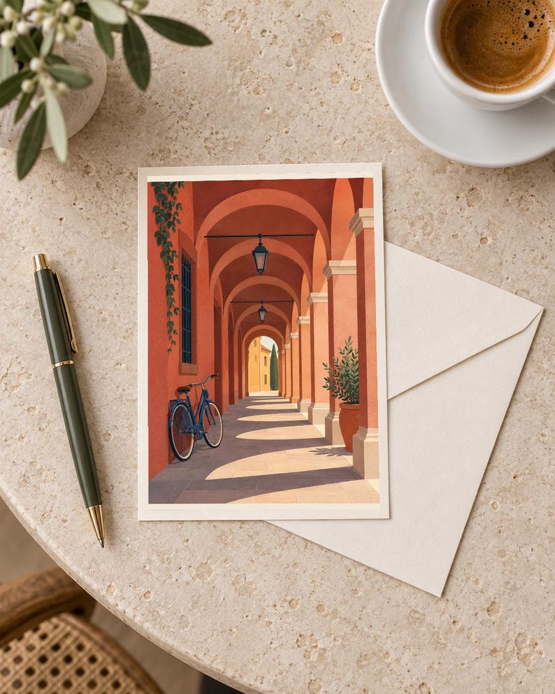 Pu&ograve; includere: Un biglietto d'auguri rettangolare con l'illustrazione di un porticato color terracotta, una bicicletta blu appoggiata a una parete, lanterne sospese e una pianta in vaso, accompagnato da una busta color crema e una penna scura.