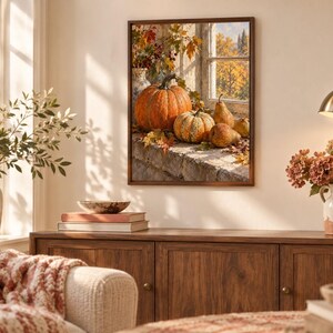 May include: A framed wall art print depicting a still life scene of orange pumpkins, gourds, and pears resting on a stone windowsill. The image features autumn foliage and a window view of trees with golden leaves, all enclosed in a dark wood frame.