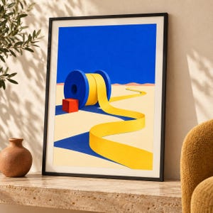 Op de afbeelding: Een ingelijste kunstdruk met een surrealistisch landschap met een grote blauwe spoel die een lang geel lint afrolt over een beige woestijnbodem. Een kleine rode kubus staat naast de spoel onder een helderblauwe lucht.