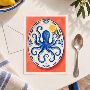 May include: A rectangular art print featuring an illustration of a blue octopus centred on an oval white plate with blue decorative borders. A single yellow lemon slice rests on the plate. The background is a solid, vibrant coral orange colour.