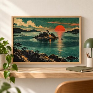 May include: A framed landscape print featuring a small island with a glowing cabin in the center of a calm, circular-rippled lake. The scene depicts a large, vibrant red sun setting over dark mountains under a teal sky with white clouds.