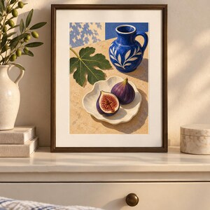 May include: A framed art print depicting a still life scene with a vibrant blue ceramic pitcher featuring white leaf patterns, a single green fig leaf, and two figs, one whole and one halved, resting on a white scalloped plate on a stone surface.