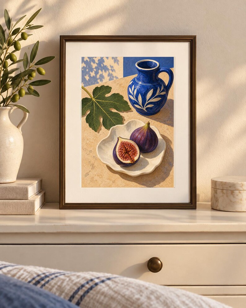May include: A framed art print depicting a still life scene with a vibrant blue ceramic pitcher featuring white leaf patterns, a single green fig leaf, and two figs, one whole and one halved, resting on a white scalloped plate on a stone surface.