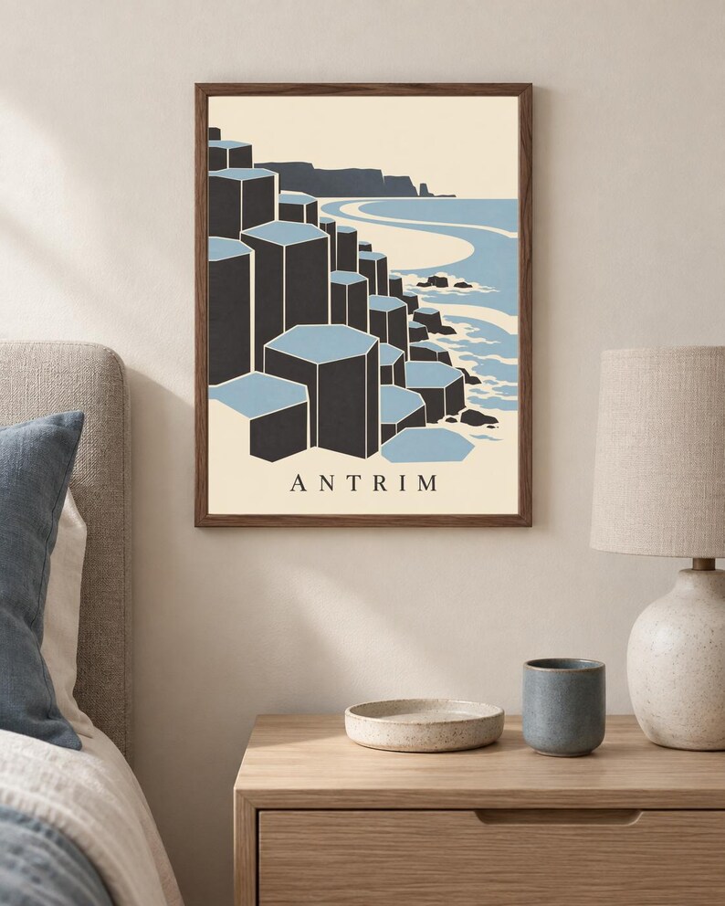 May include: A framed wall art print featuring a stylised illustration of the Giant's Causeway in Antrim. The graphic depicts dark grey hexagonal basalt columns against a light blue sea and cream background, with the text ANTRIM printed at the bottom.