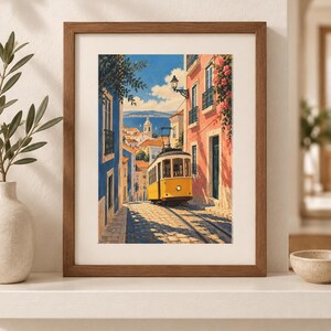 K&ouml;nnte beinhalten: Ein gerahmter Kunstdruck, der eine gelbe Stra&szlig;enbahn auf einer gepflasterten Stra&szlig;e zwischen blauen und rosafarbenen Geb&auml;uden zeigt. Die Szene umfasst einen Blick auf das Meer in der Ferne unter einem klaren blauen Himmel mit gr&uuml;nem Blattwerk.