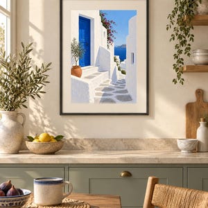 Puede incluir: Una l&aacute;mina de arte enmarcada que representa una escena mediterr&aacute;nea con edificios de piedra blanca, una puerta azul brillante, una maceta de terracota con un &aacute;rbol peque&ntilde;o, flores rosas y vistas al mar azul bajo un cielo despejado.