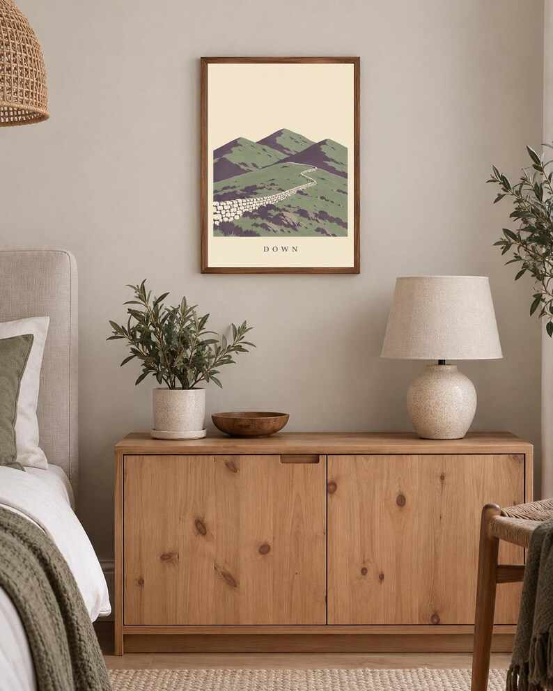 Pu&ograve; includere: Una stampa artistica da parete incorniciata che presenta un'illustrazione paesaggistica stilizzata di montagne verdi e un muro di pietra che si snoda tra le colline. L'opera ha uno sfondo color crema e la parola DOWN stampata in nero al centro in basso.