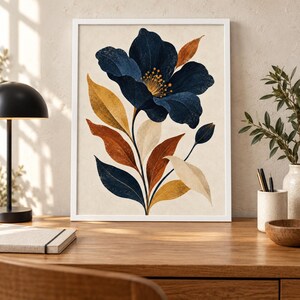 May include: A framed wall art print featuring a large, dark navy blue flower with a yellow centre, surrounded by elongated leaves in shades of mustard yellow, burnt orange, cream, and navy blue, set against a light beige background.