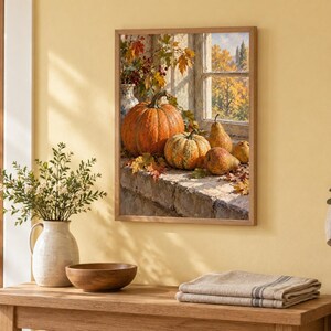 May include: A framed wall art print depicting a still life scene of a large orange pumpkin, a smaller striped pumpkin, and two pears resting on a stone ledge. The background shows a window view of autumn trees with golden foliage and sunlight.