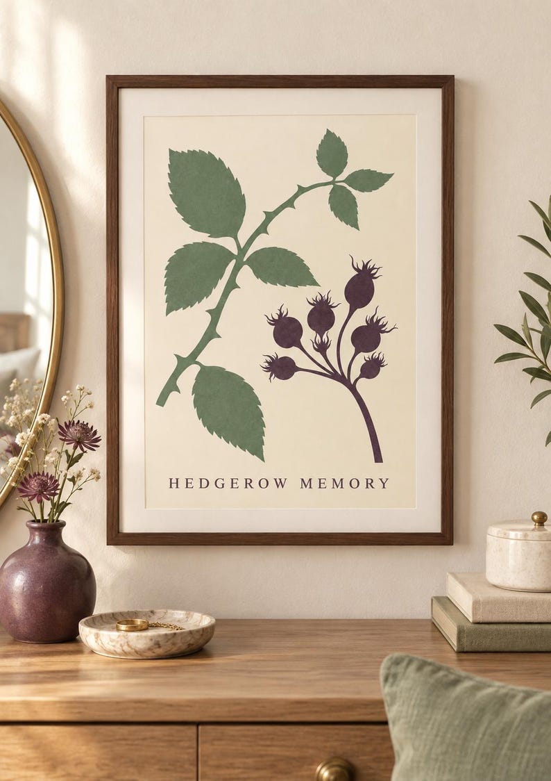 May include: A framed wall art print featuring a botanical illustration of green leaves and dark purple rose hips on a cream background. The text HEDGEROW MEMORY is printed in black at the bottom center of the print, which is enclosed in a dark wood frame.