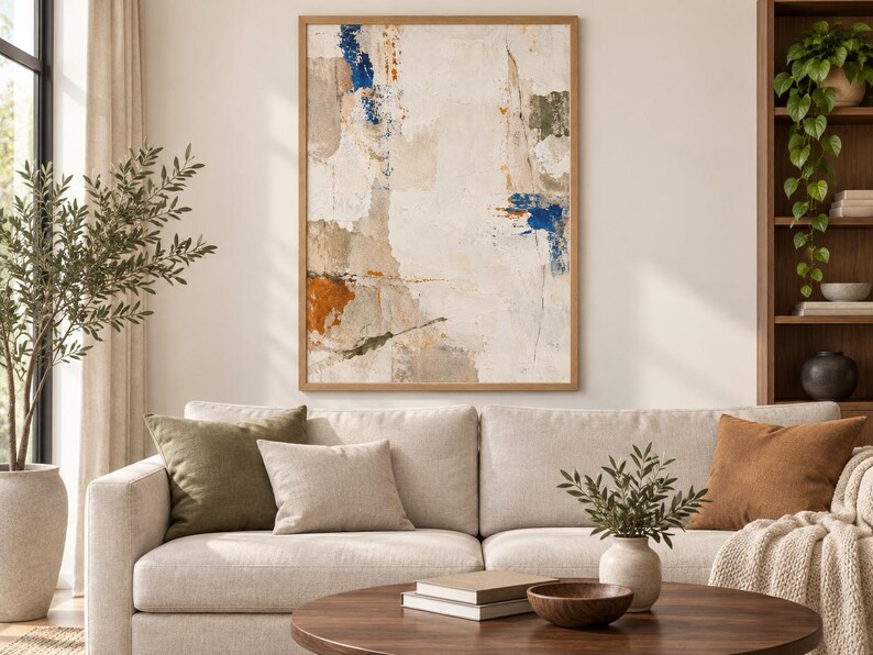 K&ouml;nnte beinhalten: Ein rechteckiges Wandbild in einem hellen Holzrahmen mit einer abstrakten Komposition aus strukturierten Schichten in Creme, Wei&szlig; und Beige, akzentuiert durch kr&auml;ftige Farbspritzer in Dunkelblau und gebranntem Orange.