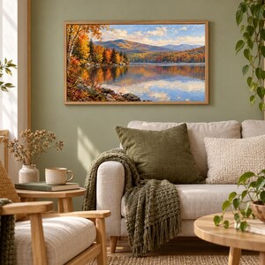 Pode incluir: Uma pintura de paisagem retangular numa moldura de madeira clara representando um lago calmo rodeado por &aacute;rvores de outono com folhagem laranja, amarela e vermelha vibrante sob um c&eacute;u azul com nuvens brancas, montada numa parede verde s&aacute;lvia.