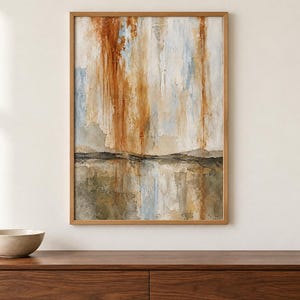 Pu&ograve; includere: Un'opera d'arte da parete rettangolare incorniciata raffigurante un dipinto paesaggistico astratto con strisce verticali color arancio bruciato, bianco e azzurro sopra una linea orizzontale scura, con toni terrosi di marrone e grigio nella parte inferiore.