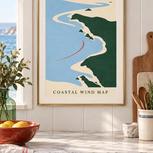 May include: A framed wall art print titled Coastal Wind Map featuring a minimalist graphic illustration of a coastline with dark green land, light blue water, a sandy beige shore, and a single curved red line indicating wind direction.