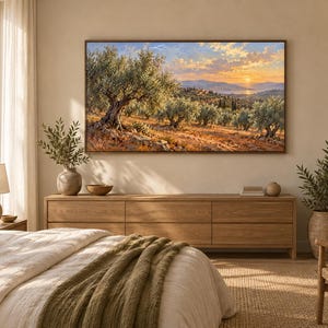 May include: A rectangular landscape painting in a thin brown frame depicting an olive grove at sunset with golden light, rolling hills, and a distant body of water. The artwork is mounted on a light beige wall above a long wooden media console.