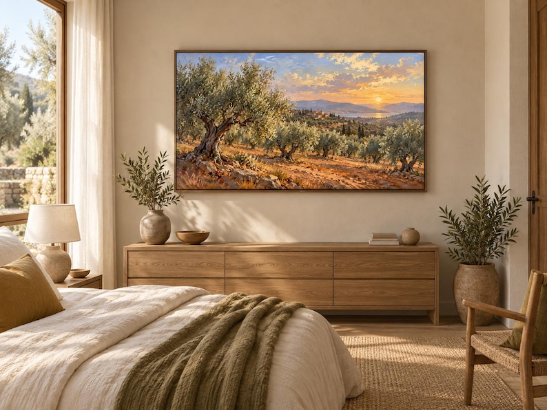 May include: A rectangular landscape painting in a thin brown frame depicting an olive grove at sunset with golden light, rolling hills, and a distant body of water. The artwork is mounted on a light beige wall above a long wooden media console.