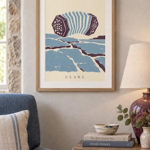 May include: A framed art print featuring a stylized illustration of a concertina floating above a blue and purple landscape. The word CLARE is printed in black capital letters at the bottom of the cream-colored background within the light wood frame.