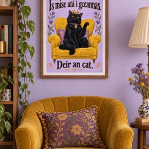 May include: A framed wall art print featuring a black cat wearing a gold crown and a purple collar with a shamrock charm, sitting on a yellow armchair. The text reads Is mise at&aacute; i gceannas and Deir an cat against a light purple background.