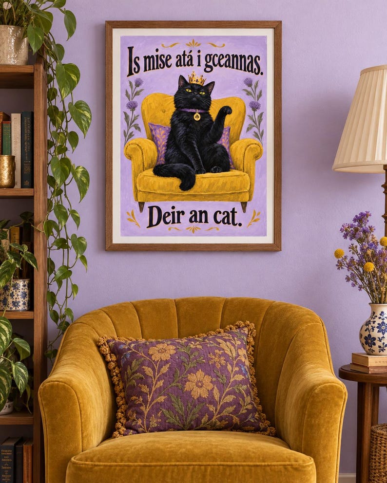 May include: A framed wall art print featuring a black cat wearing a gold crown and a purple collar with a shamrock charm, sitting on a yellow armchair. The text reads Is mise at&aacute; i gceannas and Deir an cat against a light purple background.