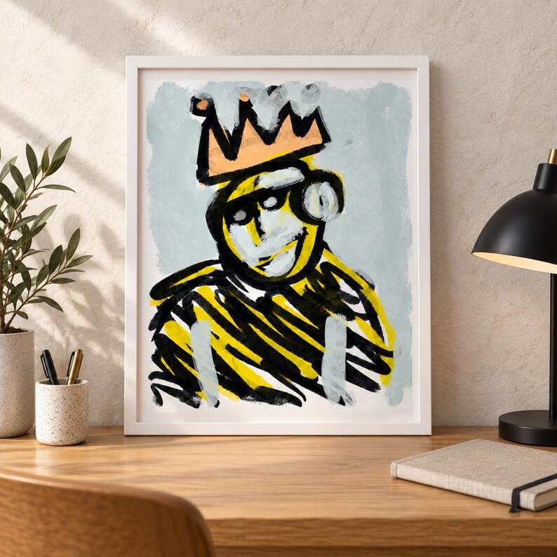 May include: A framed wall art print featuring an abstract, expressive painting of a figure wearing a peach-colored crown. The artwork uses bold, gestural brushstrokes in black and yellow against a pale blue background, set in a white frame.
