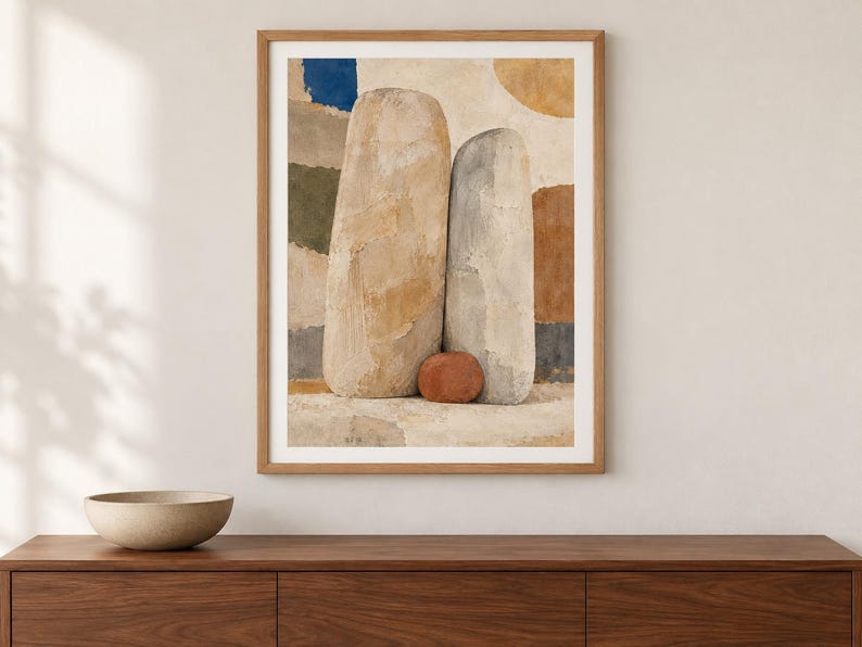 May include: A framed wall art print featuring an abstract composition of two tall, textured, beige and gray stone-like forms standing side-by-side, with a small, rounded, terracotta-colored object at their base against a background of muted color blocks.