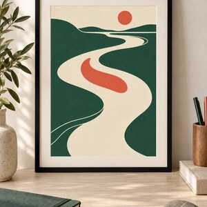May include: A framed wall art print featuring a stylized landscape with a winding cream-colored river flowing through dark green hills under a pale sky. A solid red sun sits near the horizon, and a red oval shape floats in the center of the river.