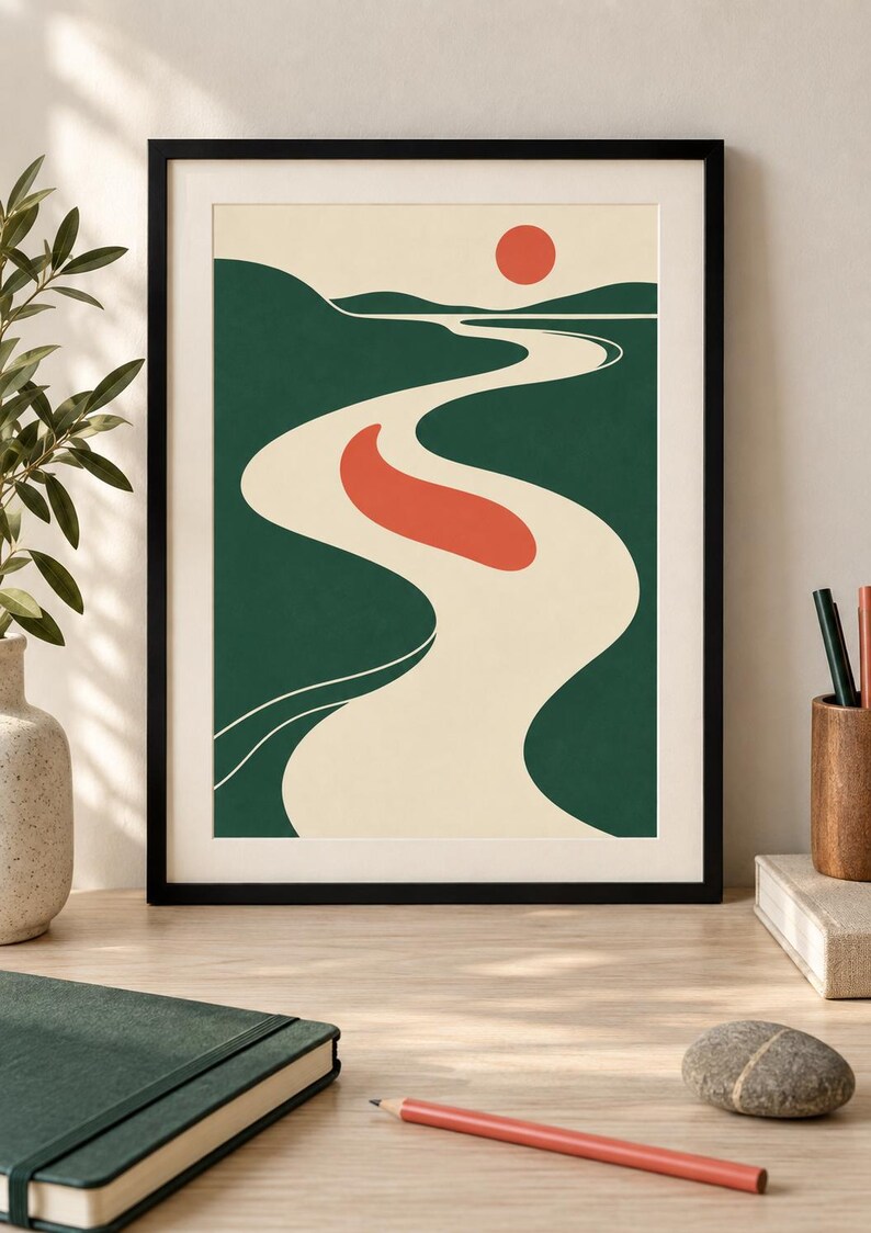May include: A framed wall art print featuring a stylized landscape with a winding cream-colored river flowing through dark green hills under a pale sky. A solid red sun sits near the horizon, and a red oval shape floats in the center of the river.