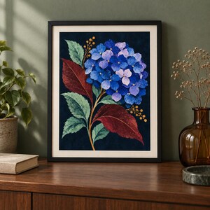 May include: A framed wall art print featuring a vibrant blue hydrangea flower cluster centred against a dark navy background. The botanical illustration includes large, textured green and deep maroon leaves, along with thin stems of small yellow berries.