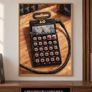 May include: A black pocket operator synthesiser featuring a digital LCD screen, multiple square buttons with red accents, and a black audio cable connected to the top right. The device displays the text robot and pocket operator on its frame.