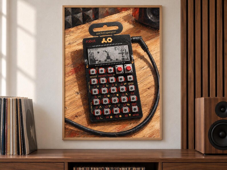 May include: A black pocket operator synthesiser featuring a digital LCD screen, multiple square buttons with red accents, and a black audio cable connected to the top right. The device displays the text robot and pocket operator on its frame.